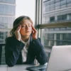 Woman at her desk with a stress headache, a physical sign of how stress affects health.