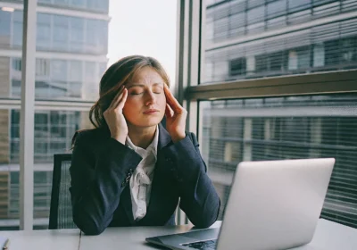 Woman at her desk with a stress headache, a physical sign of how stress affects health.